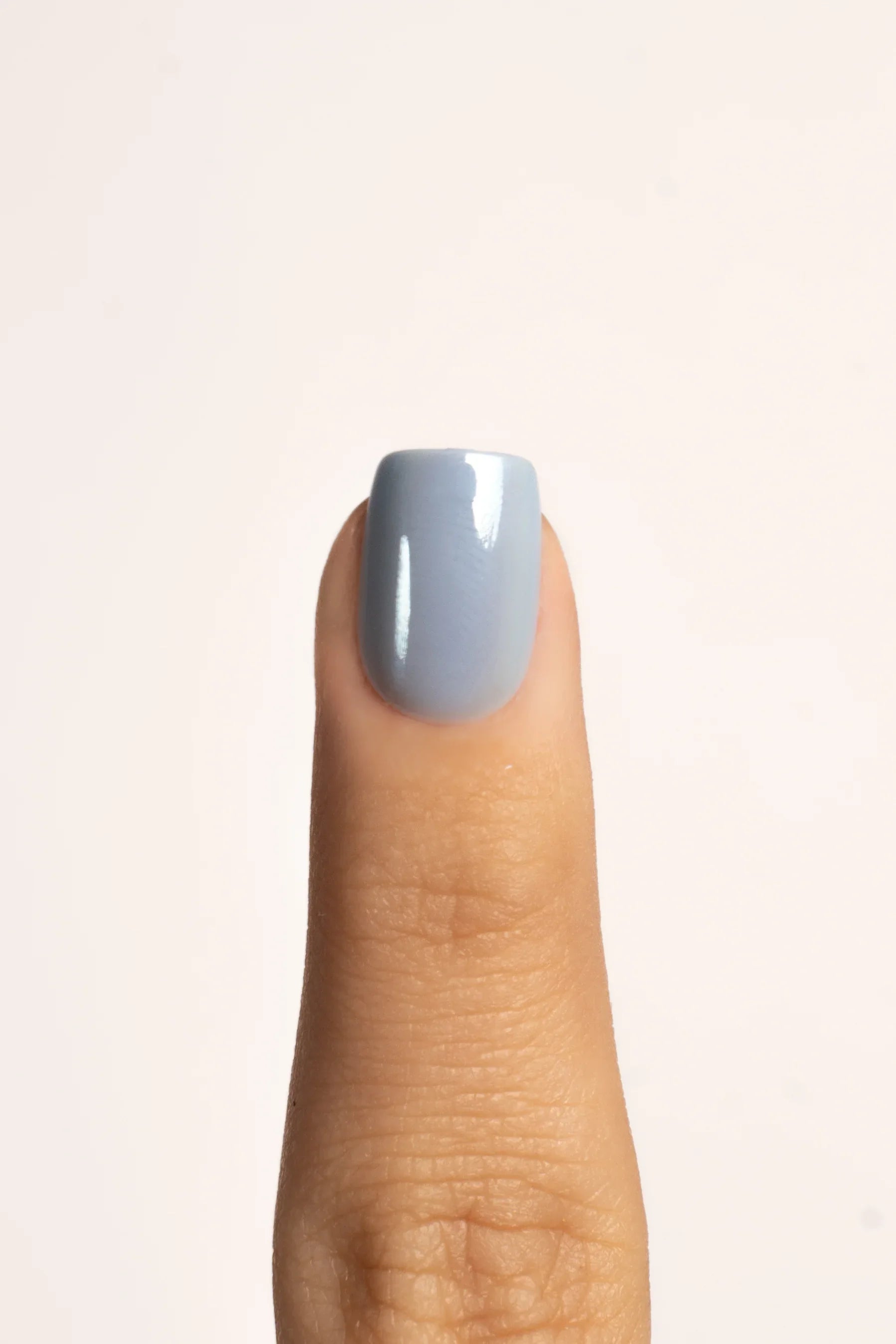 Nahaufnahme eines Daumens mit hellblau glänzendem FlexiGel Press On Nagel, neutrale Kulisse