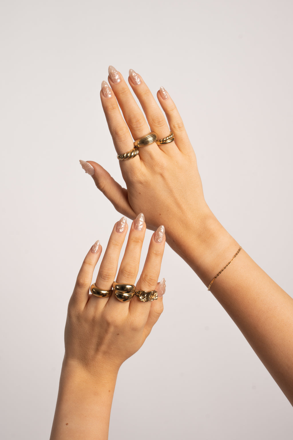Hände mit FlexiGel Press-On Nails in Crystal Glow – schimmerndes Nude mit Champagner-Glanz und Goldschmuck von Nailish