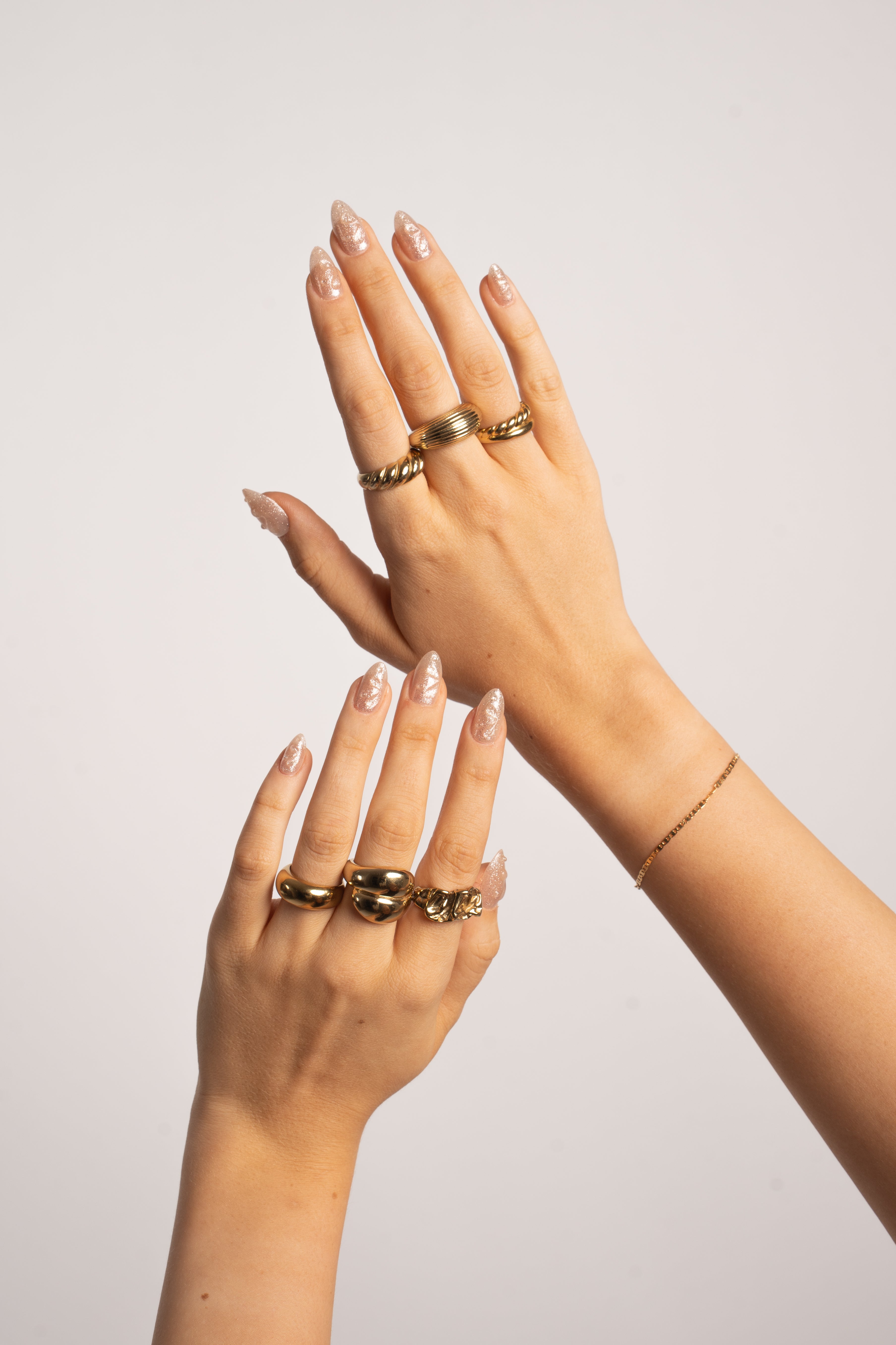 Hände mit FlexiGel Press-On Nails in Crystal Glow – schimmerndes Nude mit Champagner-Glanz und Goldschmuck von Nailish