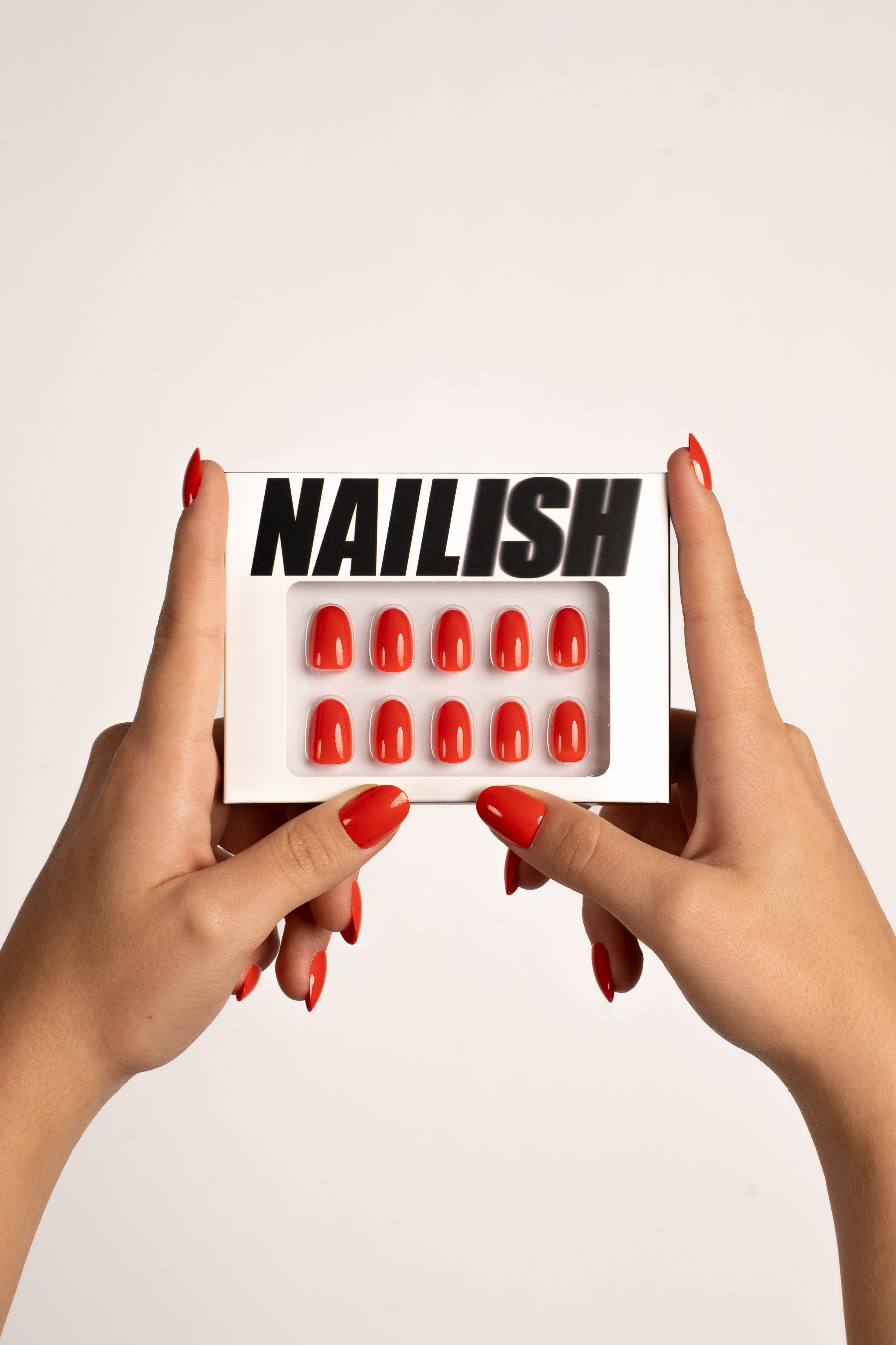 Hände halten Nailish Verpackung mit Red Crush Soft Gel Press-On Nails – leuchtendes Rot in Rundform