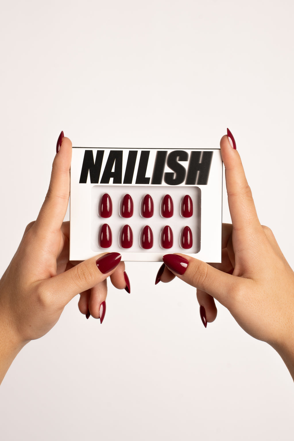 Hände halten Nailish Verpackung mit Ruby Night FlexiGel Press-On Nails – tiefes Dunkelrot in Mandelform