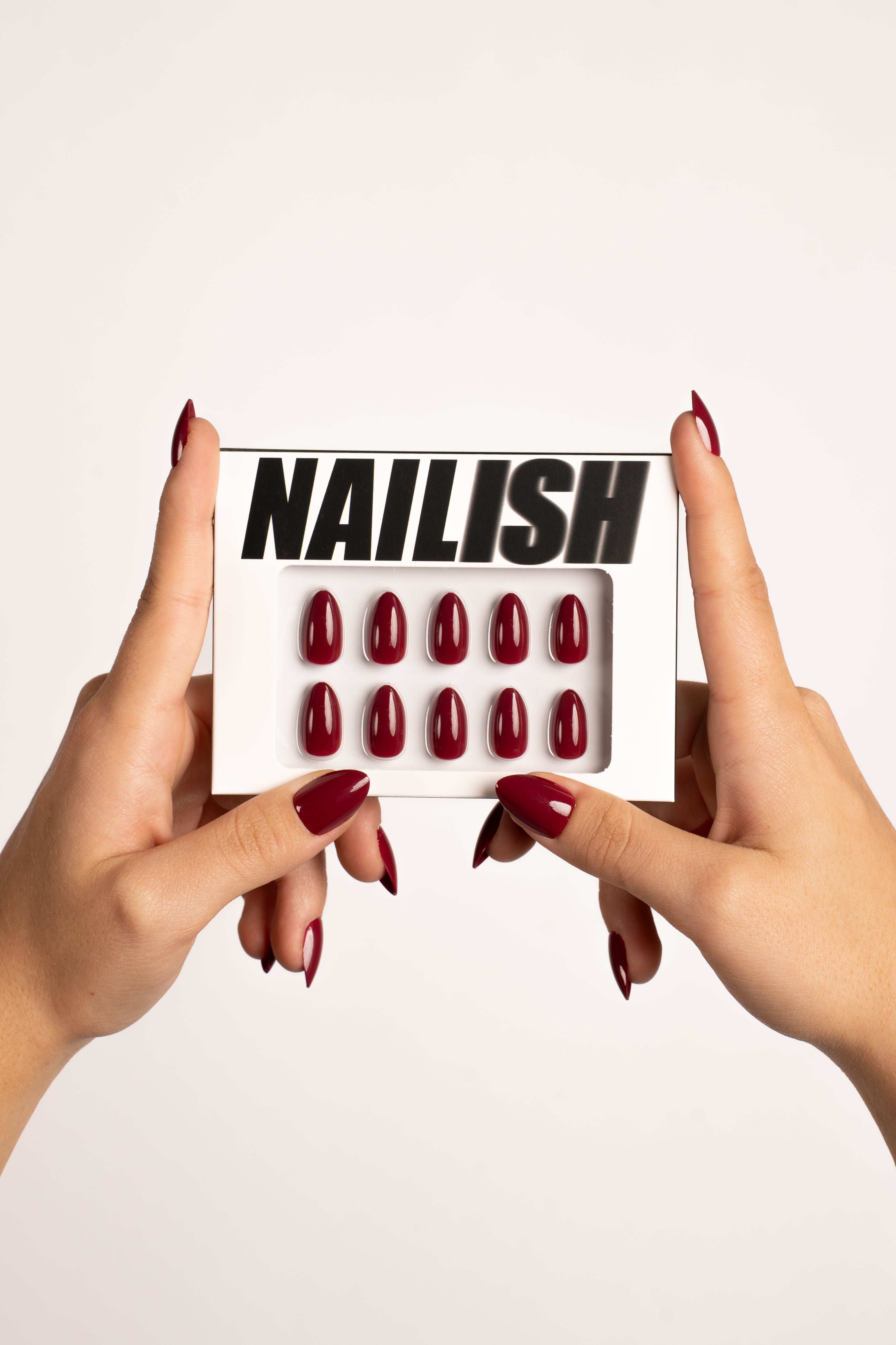 Hände halten Nailish Verpackung mit Ruby Night FlexiGel Press-On Nails – tiefes Dunkelrot in Mandelform